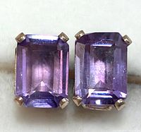 Close-up front view of a pair of silver stud earrings each set with a rectangular faceted amethyst stone held by four prongs.