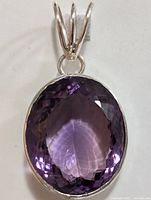 Front view of an oval faceted purple amethyst set in silver with triple bail.