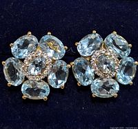 Close-up image showing front view of silver earrings with blue topaz stones and clear accent stones in floral cluster design.