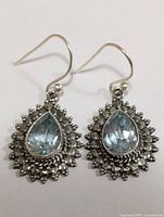 Front view of pair of silver earrings with pear-shaped blue topaz stones and detailed silver framing.