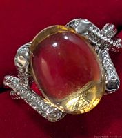 Close-up front view of the silver citrine ring showing the large oval cabochon stone and detailed silver prongs against a red background.