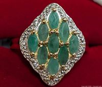 Close-up view of silver ring with nine marquise-cut emerald stones arranged in a cluster, showing green color and gold-tone prong settings with small clear stones around the perimeter.