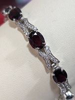 Close-up photo of the silver bracelet showing oval garnet stones set with prongs and clear stone accents.
