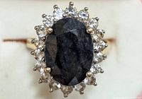 Close-up front view of the silver ring with dark oval gemstone center and halo of clear stones.