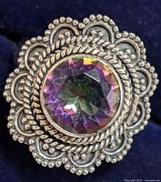 Close-up image of a silver marcasite ring featuring a large faceted purple center stone with intricate silver beaded and rope design around it.