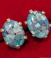 Close-up photo of a pair of silver earrings with oval-shaped opalite stones in mosaic inlay design set with silver prongs on a red background.