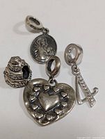 Photo showing a collection of four silver Pandora charms arranged on a plain surface, clear details on different charm designs.