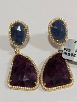 Front view of the silver earrings showing faceted blue sapphires with bordering cubic zirconia and large ruby drops also bordered with cubic zirconia.