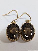 Front view of both silver earrings with oval faceted smokey quartz stones set in gold bezels, hooked style.