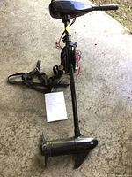 Full view of the black electric outboard motor laying on the ground with attached carrying strap and owner’s manual beside it.