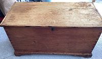 Front view of the primitive pine chest showing the full rectangular shape, natural wood grain, and base with caster wheels.