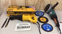 Dewalt reciprocating saw with power cord, instruction manual, two spare saw blades, original yellow Dewalt box, and four abrasive discs laid out on wood background.