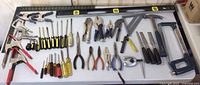 Wide view showing the full collection of hand tools including screwdrivers, clamps, chisels, pliers, levels, hammer, and a coping saw laid out on a white surface.