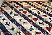 Full view of quilt laid flat showing diagonal pattern of log cabin blocks, hearts, stars and flags