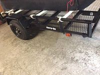 Side view of trailer frame showing mesh floor, side rails, single axle wheel and “Carry-On” logo