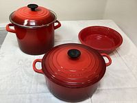 Overview of two red Le Creuset enameled pots with lids and a red Fiesta serving bowl on table