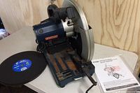 Front-right view of chop saw mounted on base, showing blade guard, handle, and rusted surface.