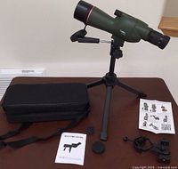 Overview of spotting scope, tripod, carrying case, adapter, lens covers, cleaning cloth, and manual laid out on table