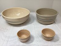 Four stoneware bowls displayed together on a white linen cloth, showing two larger bowls at the back and two smaller ones in front.