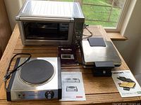 Photo showing all three appliances: Breville toaster oven, Cuisinart waffle maker, and Cuisinart countertop burner placed on a wooden surface near a window.