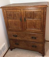 Front view of oak cabinet showing two upper paneled doors and two lower drawers with brass handles.