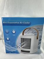 Box shows the mini evaporative air cooler with airflow icons indicating cool, light, and humidify features.