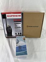 Three boxes containing new portable two-way radios: Baofeng BF-888S, Idradio in plain brown box, and Retevis RT32 model boxes.