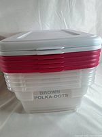 Stack of plastic storage containers with clear bases and white and red lids. One container labeled 'BROWN POLKA-DOTS'.