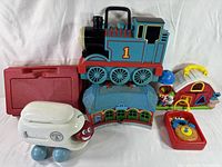 Overview photo of assorted vintage children's toys including toy train, airplane, phone, barn, figure, and red case