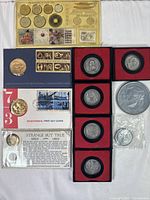 Full view of vintage coin collection including individual coins, commemorative medals, coin sets, first day cover, and informational card with coins in holders, sleeves, and display packaging.