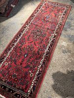 Full view of the long rectangular runner rug showing the overall red floral patterned design and borders on concrete floor.
