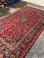 Angled full view of rug on concrete floor showing red field and medallion design