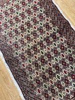 Full view of the Turkmen backrest rug showing geometric diamond and cross pattern in muted red, green, cream, and black.