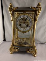 Front view of the brass crystal regulator clock showing ornate brass decorations and clock face with visible wear.