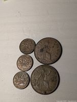 Five coins lying flat on a surface, including three Canadian pennies and two Great Britain pennies.