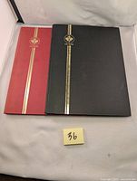Two vintage Uni-Safe brand stamp albums, one red, one black, lying closed on a white surface with a lot number 36