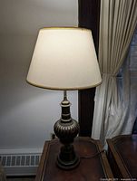 Photo showing front and side view of the antique brass lamp with white shade illuminated.