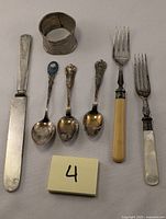 Top view of entire collection showing all spoons, forks, and napkin ring on a neutral surface with item number 4