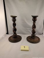 Pair of antique barley twist oak candlesticks on flat circular bases with brass tops, standing side-by-side with a measuring tape showing height.