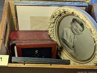 Overview of box containing various picture frames including oval ornate frame with vintage child photo
