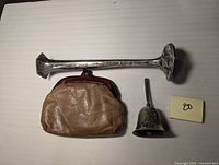 Photo showing all three items: long candlestick, leather coin purse, and small bell.