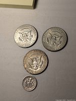 Four US coins arranged on flat surface: three Kennedy half dollars and one Roosevelt dime. Coins show obverse and reverse sides, clear date and details visible on all coins.