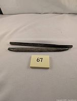 Two tarnished silver tie bars lying flat with a small post-it note marked '67'.