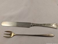 Cutting knife and oyster fork laid on white cloth, showing the full knife blade and the three-tined fork