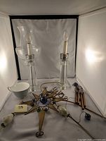 Photo showing two glass lamps with candle-style bulbs, a ceramic teacup, decorative stained glass star ornament, and wind chime parts laid out.