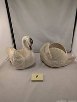 Photo of two ceramic swan planters side by side, one with black head and visible wear on feet, the other all white with crazing.