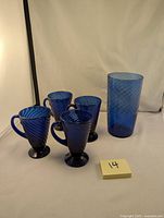 Photo showing one large cobalt blue tumbler and four small matching sipping mugs with a swirl design, all made of hand blown glass.
