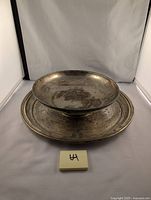Image showing the footed silver plated bowl placed on top of the round silver plated plate, both showing signs of wear and tarnish typical of vintage silver plating.