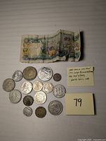 Lot shows various world coins with a folded one dollar banknote from The Central Bank of The Bahamas placed above them.