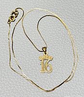 Yellow gold 'Sweet 16' pendant necklace laid out flat on white textured surface showing full chain and clasp with pendant centered.